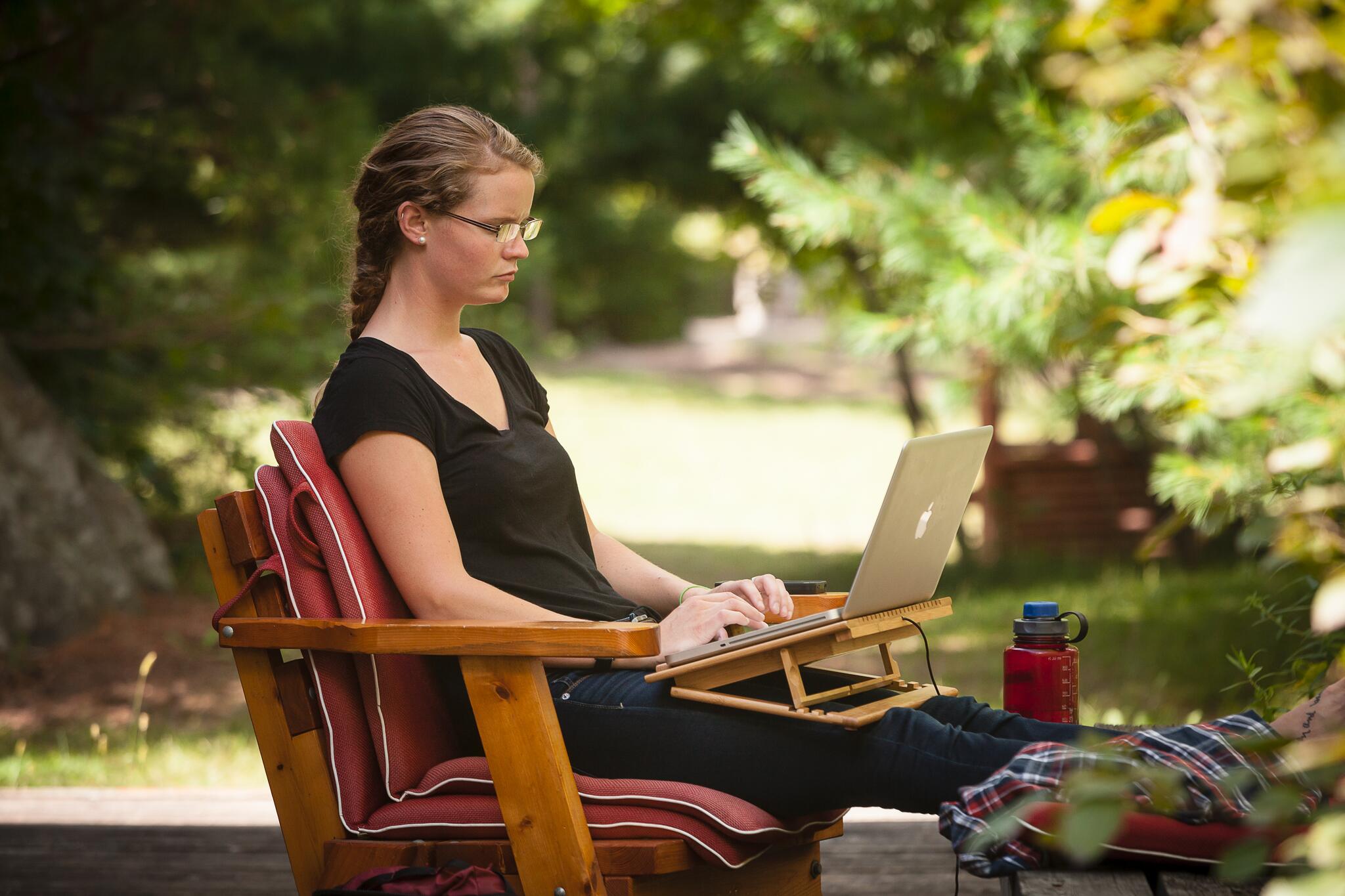 A student sitting on her porch working on her laptop